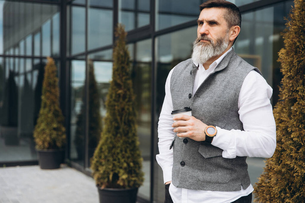 Brutal bearded gray-haired senior man drinking coffee on urban clean spaces - Photo, Image