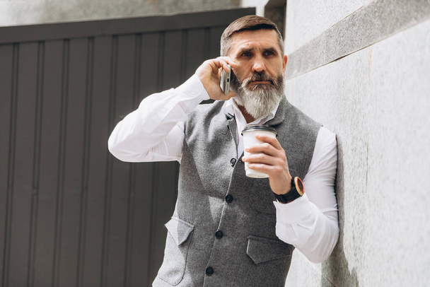 Un hombre mayor de pelo gris barbudo usa y habla en un teléfono inteligente - Foto, imagen