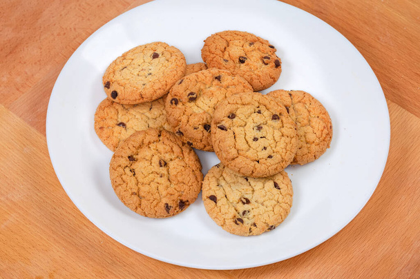 Biscuits aux pépites de chocolat à base de farine d'avoine sur le plat blanc sur une surface en bois - Photo, image