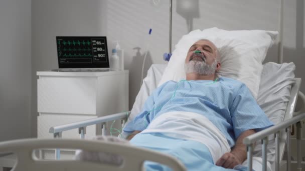 An elderly patient wakes up coming out of a coma. Open your eyes while lying on a bed in a hospital connected In the Hospital Sick Male Patient Sleeps on the Bed, . - Materiaali, video