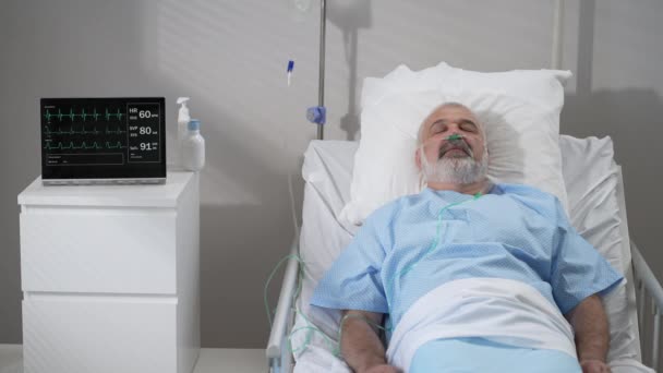 An elderly patient wakes up coming out of a coma. Open your eyes while lying on a bed in a hospital connected In the Hospital Sick Male Patient Sleeps on the Bed, . - Video