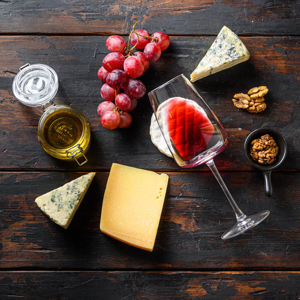 Uvas frescas, vino tinto, quesos franceses, miel y nueces sobre madera envejecida rústica. Vista superior con cultivo cuadrado. - Foto, imagen
