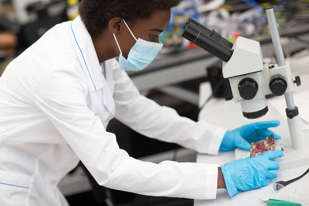 Bilimadamı Afrikalı Amerikalı kadın laboratuarda elektronik aletlerle çalışıyor. - Fotoğraf, Görsel