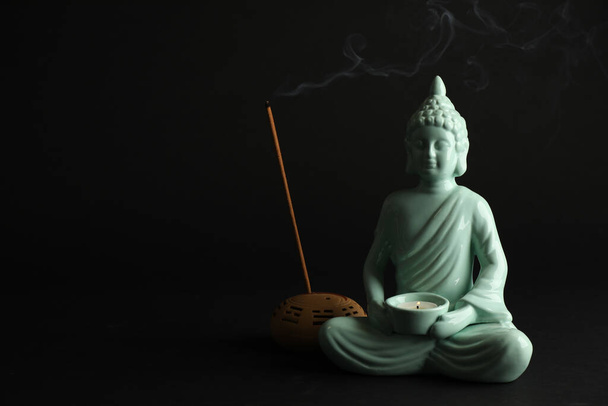 Beautiful ceramic Buddha sculpture with burning candle and incense stick on black background. Space for text - Фото, зображення