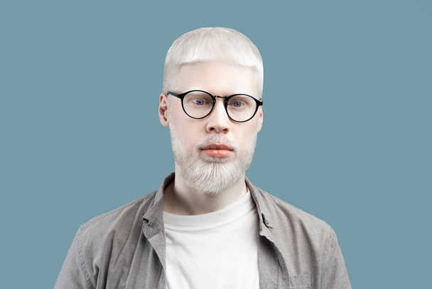 Portrait of serious albino man with pale skin and blue eyes, wearing eyeglasses against turquoise studio background - Photo, Image