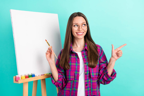 Portrait of trendy beautiful cheerful girl drawing new picture showing copy space isolated over bright teal color background - Valokuva, kuva