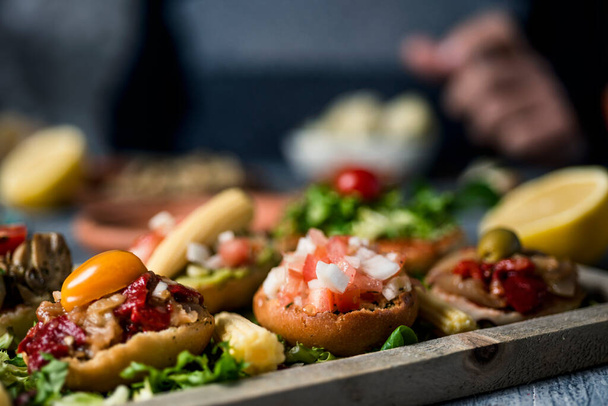 some different vegan appetizers, with different toppings, on a wooden tray, on a gray rustic wooden table, and a man sitting at the table in the background - Foto, immagini