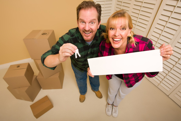 Goofy Couple Holding Keys et Blank Sign in Room avec boîtes en carton emballées
. - Photo, image