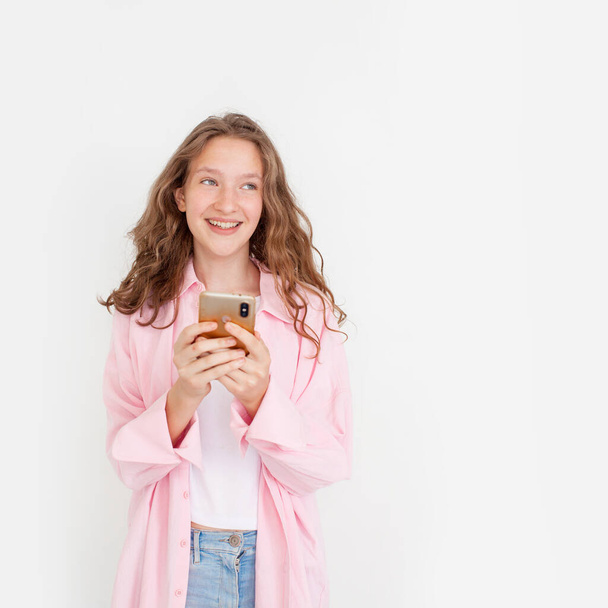 Happy Teen Using mobile phone and looking sideways Cheerful young woman girl in pink shirt posing isolated on white wall background studio portait. People lifestyle concept - Photo, image