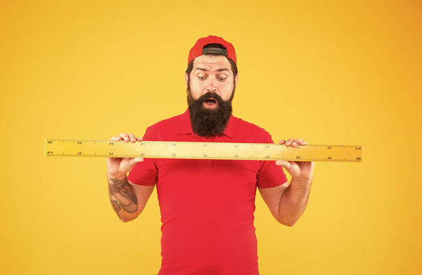 Big size. Measuring tool. Man holding ruler on yellow background. Bearded man preparing for maths. Hipster man in cap with big measuring instrument. Size of parcel. Post office worker with ruler - Фото, зображення