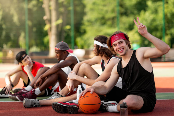Happy young basketball player and his multinational team having rest at outdoor arena, copy space - Photo, Image