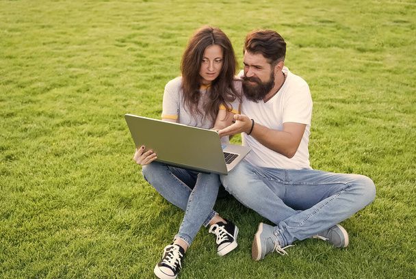 Cheerful couple use laptop sit green grass, open air office concept - Fotoğraf, Görsel