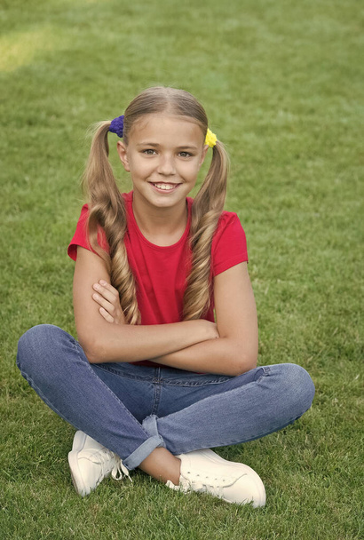 Little girl cute ponytails hairstyle relaxing on green grass, child care concept - Фото, зображення
