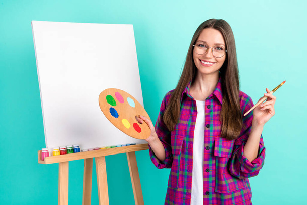 Portrait of attractive cheerful girl painting picture design oil isolated over bright teal green color background - Valokuva, kuva