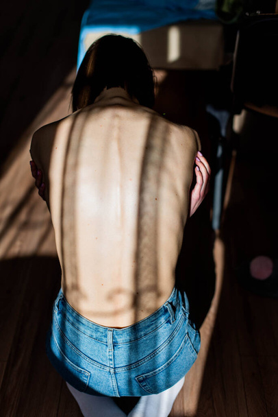 Ένα κορίτσι με ανορεξία γυρισμένη πλάτη, σπονδυλική στήλη και πλευρά ορατά. Τόνοι σε ψυχρούς τόνους για δραματικό αποτέλεσμα. - Φωτογραφία, εικόνα