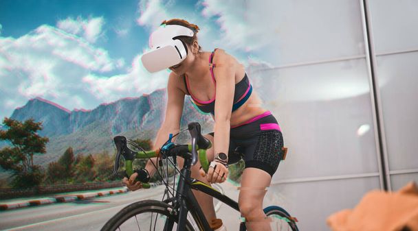 Mulher treina em casa em uma bicicleta estacionária vestindo VR-fone de ouvido. - Foto, Imagem