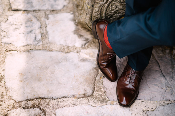 Crossed legs of a man in blue pants, red socks and brown shoes standing on the stone road, top view - Foto, immagini