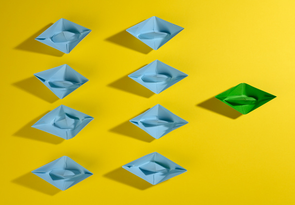 a group of blue paper boats and one green led on a yellow background. The concept of a strong leader, manipulation of the masses, a close-knit team and effective management - Foto, afbeelding