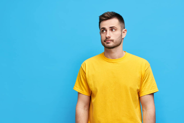 Doubtful thoughtful man looking aside to copy space over blue background - Фото, изображение