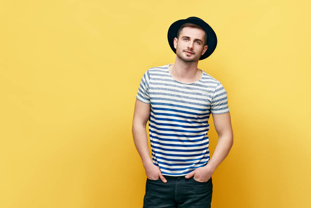 Fashion portrait of young hipster man in hat over yellow background - 写真・画像