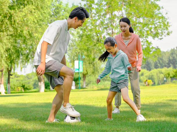 Happy family of three playing football in the park - 写真・画像