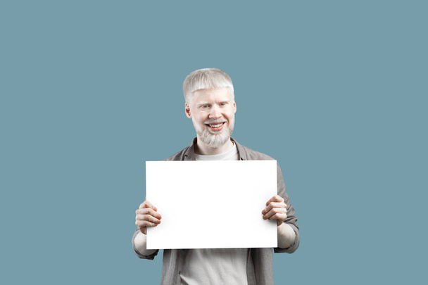 Cool offer. Happy albino guy holding blank poster with empty space, standing over turquoise studio background - Foto, immagini