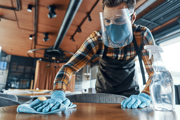 Busy man in protective face shield cleaning table in restaurant - Foto, Imagem