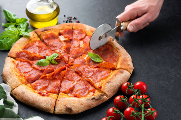 Slicing pepperoni pizza on black concrete background - Fotoğraf, Görsel