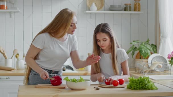 madre caucásica ama de casa enseña adolescente hija colegiala niño muestra cómo cortar verduras tomates rojos preparar ensalada vegetariana fresca, familia cocina almuerzo cena en la cocina en casa juntos - Metraje, vídeo