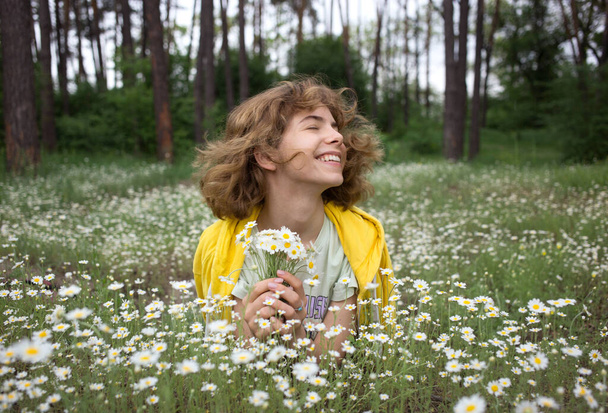 menina adolescente alegre feliz com cabelo desarrumado senta-se entre o campo com flores de camomila. Descanse em um prado florescente de floresta. Aproveite seu momento feliz, pensamento positivo, sonho acordado agradável - Foto, Imagem