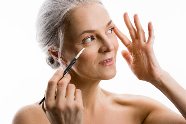 Woman with grey hair holding brush and pulls the skin with her hands - Foto, Imagen