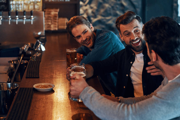 Carefree young men in casual clothing drinking beer and bonding together while sitting in the pub - Foto, Imagem