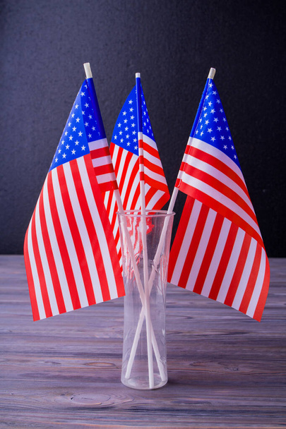 Vertical shot vase of three US flags on grey wooden desk background. - Φωτογραφία, εικόνα