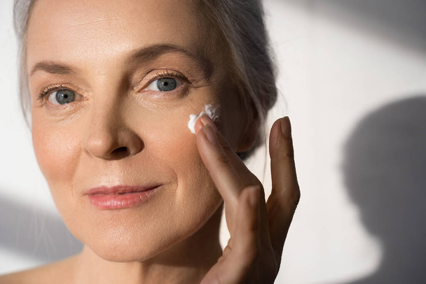 Female person applying rejuvenation cream on face with her hand - Фото, зображення