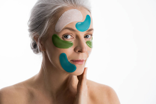 Elderly woman with a lot of beauty patch masks for eyes at her face - Foto, afbeelding