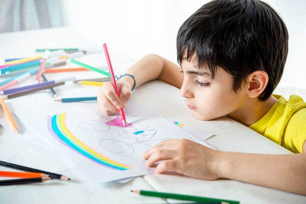 regard attentif d'un jeune garçon brun tout en dessinant à la maison sa propre idée d'une famille - Photo, image