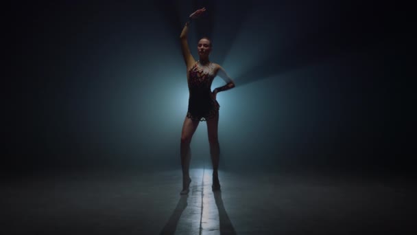 Gymnast girl standing with raised hand dark space. Sportswoman posing indoors.  - Footage, Video