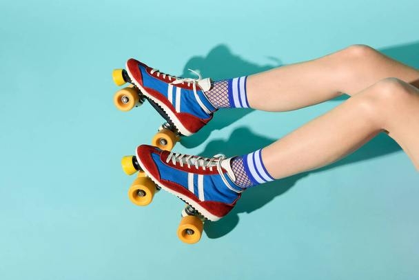 Young woman with thin skinny legs wearing colorful roller skates with yellow wheels and a view of her legs extending from the right over a blue background with copyspace - Foto, afbeelding