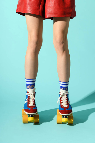 Legs of a slender sporty woman wearing multicolored roller skates and red summer shorts over a blue studio background with shadow - Foto, Imagen