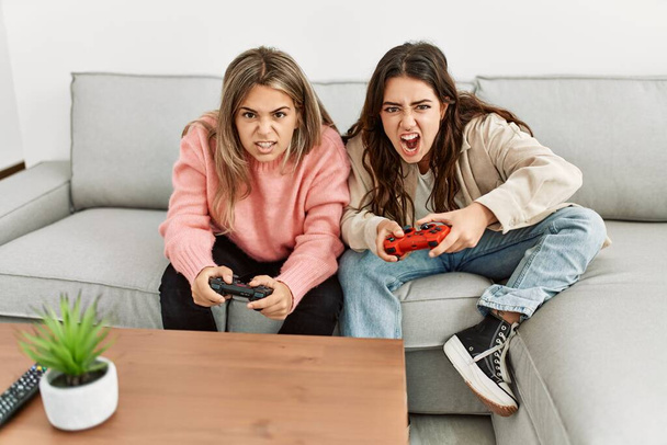 Νεαρό ζευγάρι ουρλιάζοντας και παίζοντας βιντεοπαιχνίδι στο σπίτι. - Φωτογραφία, εικόνα