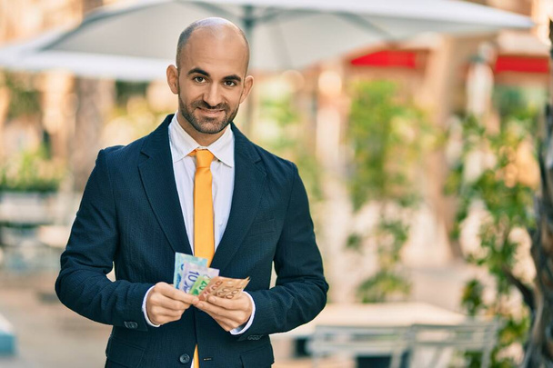Nuori latino kalju liikemies hymyilee onnellinen laskettaessa Kanadan dollareita seteleitä kaupungissa. - Valokuva, kuva
