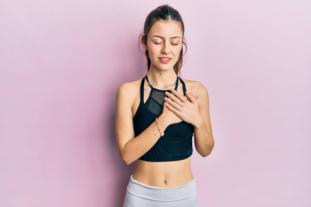 Young brunette woman wearing sportswear smiling with hands on chest with closed eyes and grateful gesture on face. health concept.  - Fotografie, Obrázek