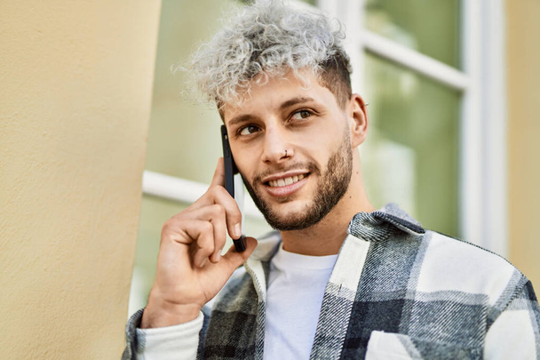 Молодий іспаномовний чоловік посміхається щасливий розмовляючий смартфон у місті
. - Фото, зображення