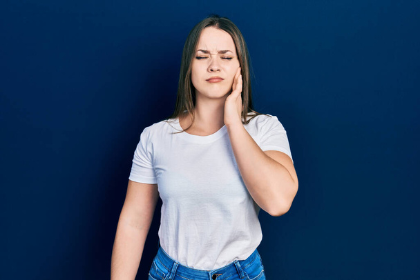 Junge hispanische Mädchen in lässigem weißen T-Shirt berühren Mund mit Hand mit schmerzhaftem Gesichtsausdruck wegen Zahnschmerzen oder Zahnerkrankungen an den Zähnen. Zahnarzt  - Foto, Bild