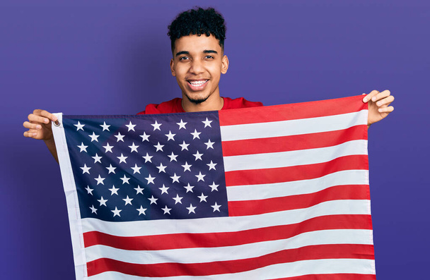 Молодой африканский американец с флагом Соединенных Штатов улыбается и громко смеется, потому что смешная сумасшедшая шутка.  - Фото, изображение
