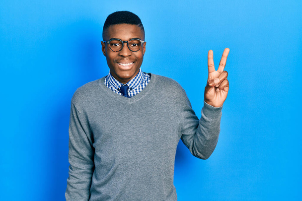 Jeune homme afro-américain portant un style d'affaires et des lunettes souriant avec un sourire heureux clin d'oeil à la caméra faisant signe de victoire. numéro deux.  - Photo, image