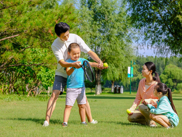Happy family of four playing tennis in the park - Zdjęcie, obraz