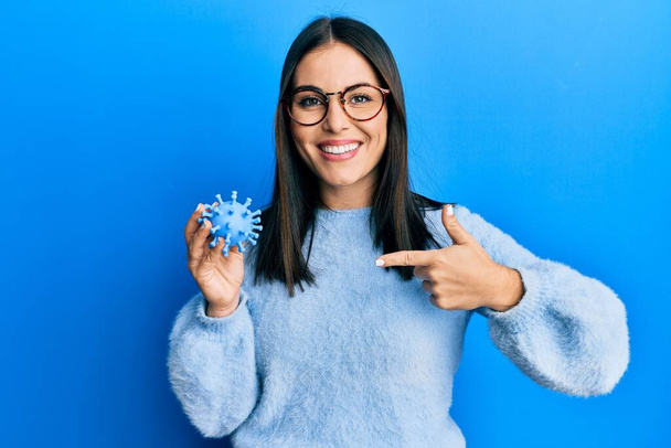 jong brunette vrouw houden virus speelgoed wijzend vinger naar een zelf lachende gelukkig en trots  - Foto, afbeelding