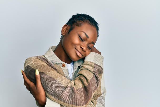 Jovem afro-americana vestindo roupas casuais abraçando-se feliz e positiva, sorrindo confiante. auto-amor e auto-cuidado  - Foto, Imagem