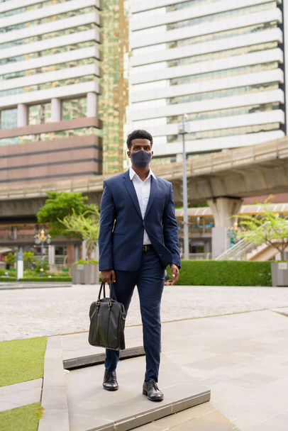 Full length shot του αφρικανού επιχειρηματία που περπατά στην πόλη φορώντας μάσκα προσώπου κάθετη βολή - Φωτογραφία, εικόνα